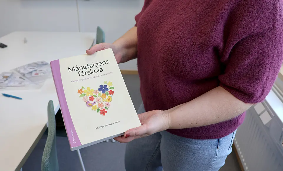 En pedagog håller upp boken "Mångfaldens förskola" av Anniqa Sandell Ring.