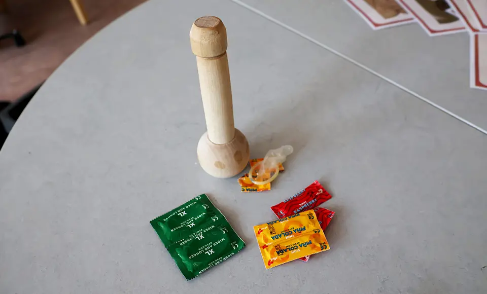 En penisatrapp i trä och kondomer som ligger bredvid.