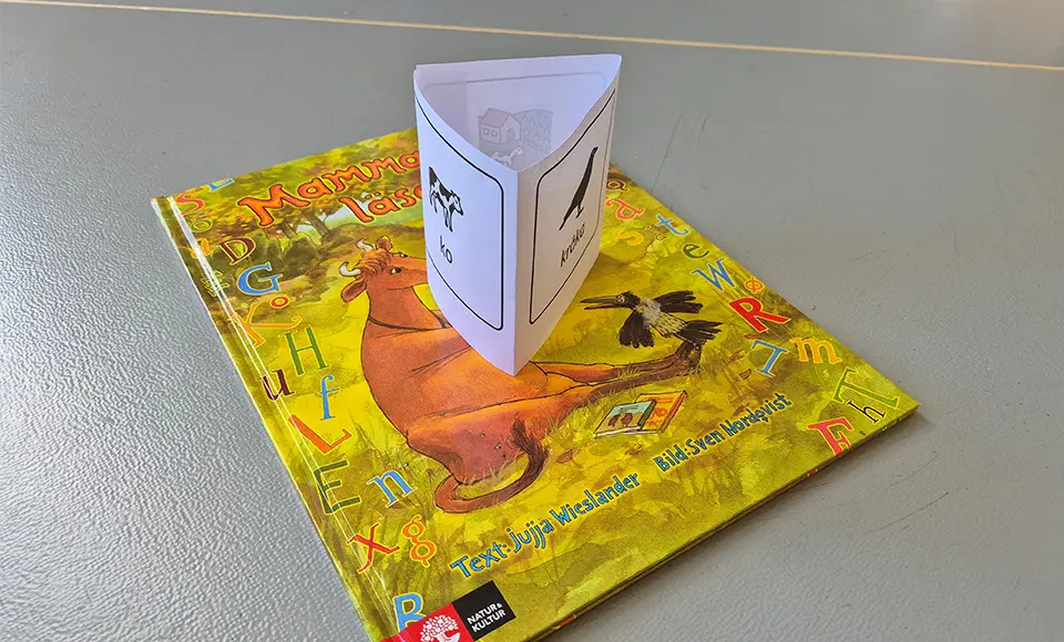 Boken Mamma Mu och Kråkan ligger ner. På boken står en skylt med Inprintbilder som visar en ko och en kråka.