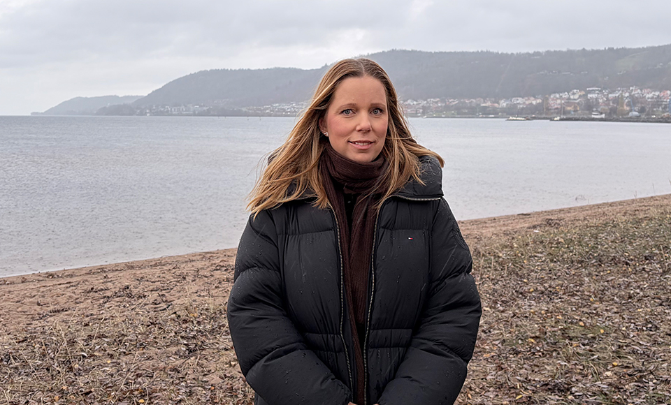 Porträttbild på Kristina Leek Kornhed som står vid en strand med Vättern i bakgrunden.