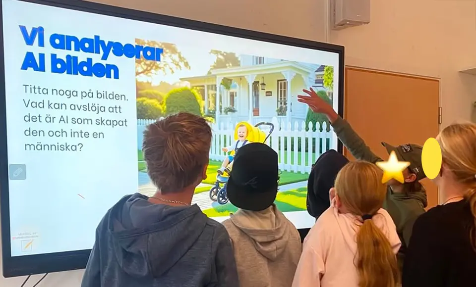En grupp elever står framför en stor skärm i klassrummet och analyserar en AI-genererad bild. På skärmen syns texten ’Vi analyserar AI-bilden’ och en bild av ett barn i vagn framför ett vitt staket och ett hus. Eleverna pekar och diskuterar detaljer som avslöjar att bilden är skapad av AI.
