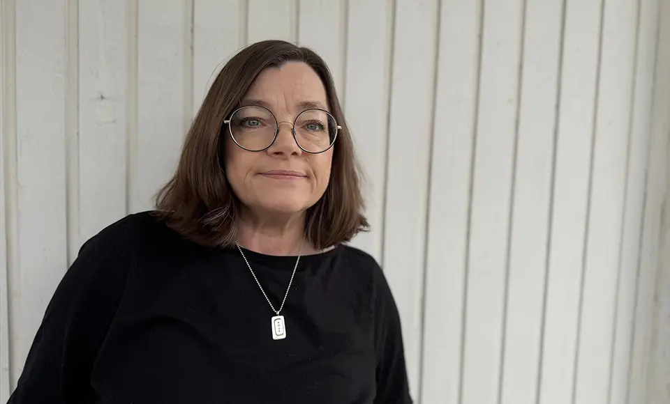 Porträttbild på Gunilla Celén som står framför en vit panelvägg.