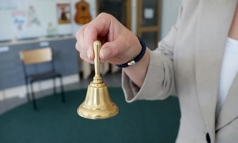 En hand som håller i en skolklocka