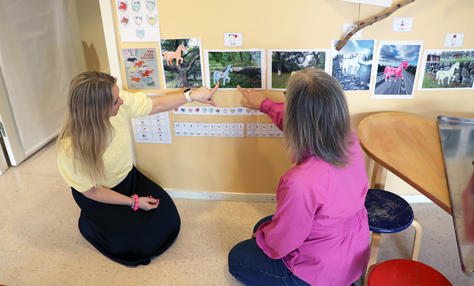 Annika och Karin sitter på golvet och tittar på bilder fårn sagan Tio vilda hästar som sitter på väggen.