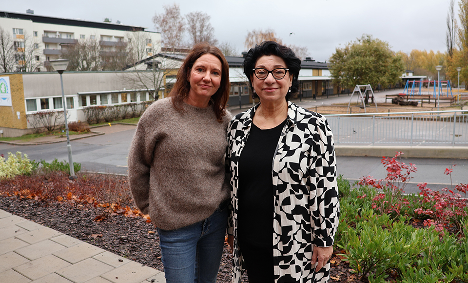 Charlotte och Amale står bredvid varandra utomhus på skolgården och tittar in i kameran.