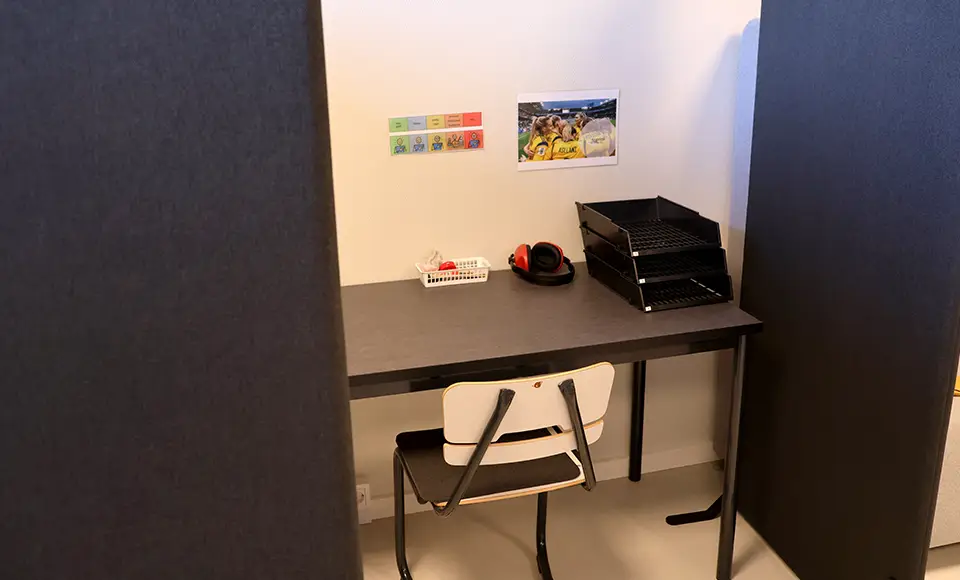 Ett skrivbord och stol som står mot en vägg. Runt omkring finns ljudisolerade väggar.