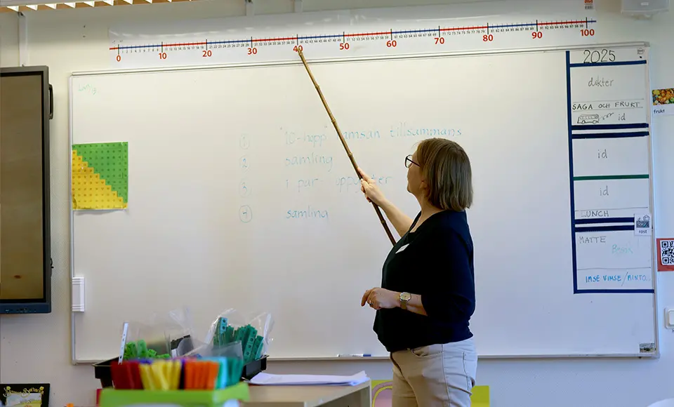 Annette står framme i klassrummet och pekar på en tallinje som sitter på väggen.